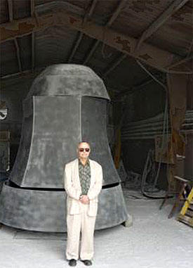 [Artist and massive bell inside barn]