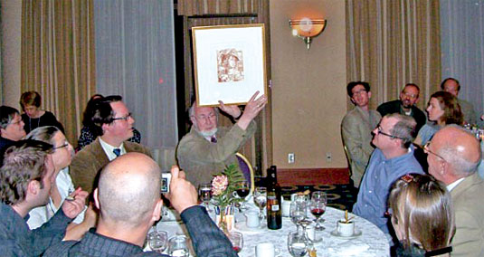 [At luncheon table, holding up certificate]