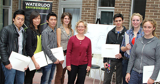 [Eight students posing with display]