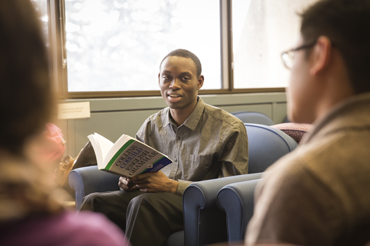 A student reads a grammar textbook in a lounge setting.