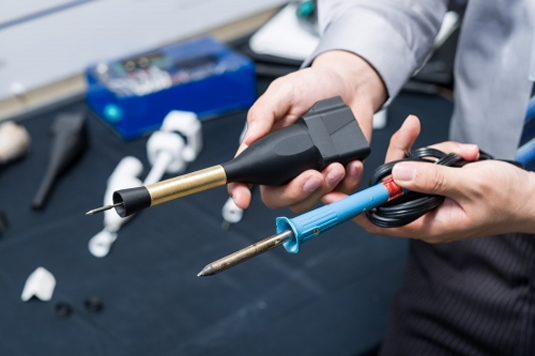 A man holds a Solder Otter and a conventional soldering iron side by side.