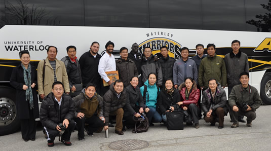 University of Waterloo athletics staff and 19 athletic directors from China stand in front of the Warriors tour bus.
